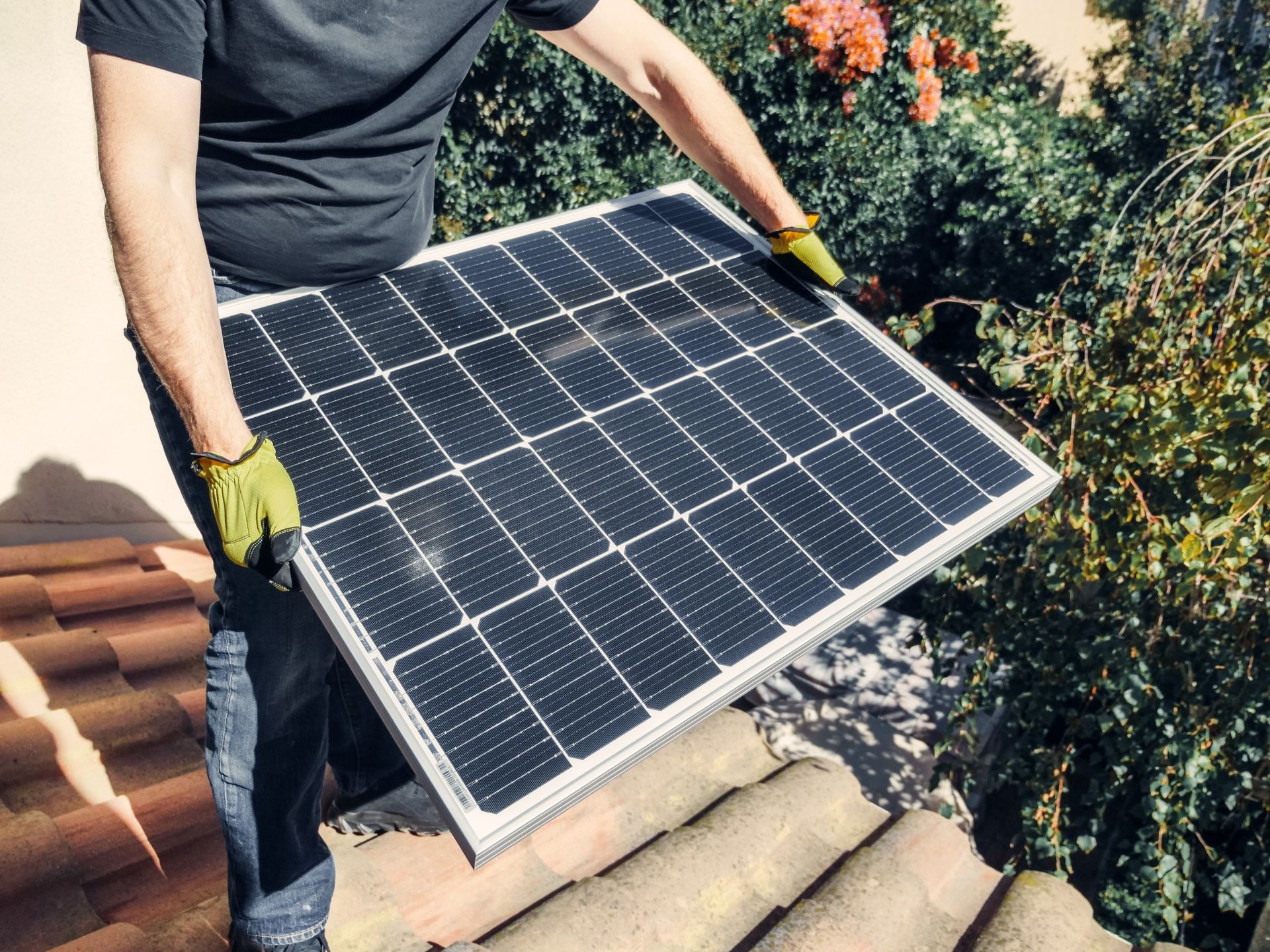 Installer carrying a solar panel across a tiled roof
